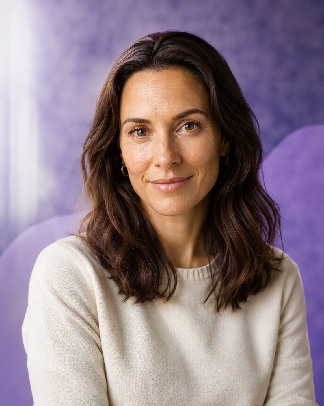Centered portrait of a smiling woman with long brown hair wearing a cream sweater against a purple background.